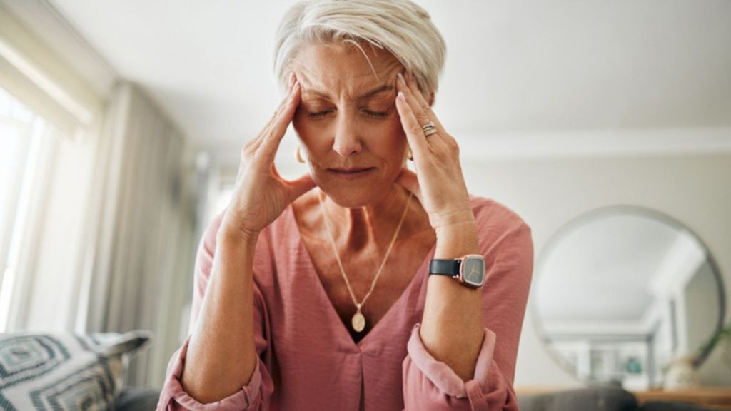 mature woman with a migraine holding her temples while sitting on a couch