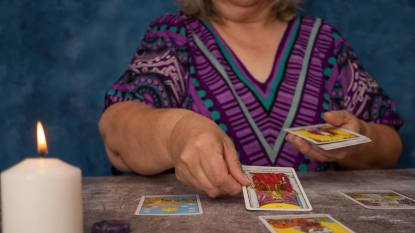 (financial tarot spread) older white-haired woman reading tarot cards on a wooden table with candle