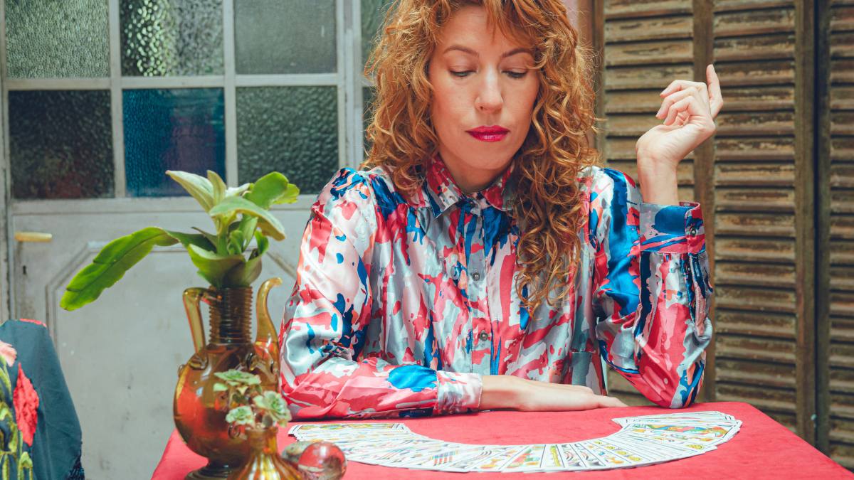 (career tarot spread) adult Argentine tarot reader woman, sitting at home looking at cards on table thinking preparing to do reading.