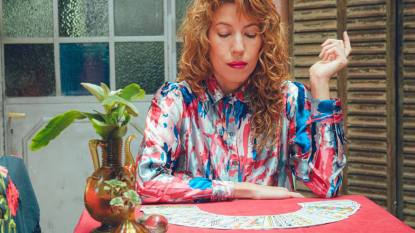 (career tarot spread) adult Argentine tarot reader woman, sitting at home looking at cards on table thinking preparing to do reading.