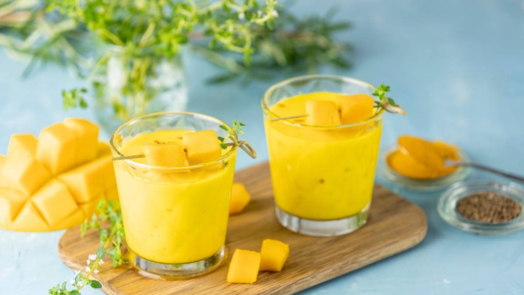Yellow Indian mango yogurt drink Mango Lassi or smoothie with turmeric and saffron. Healthy probiotic Indian cold summer drink on blue background