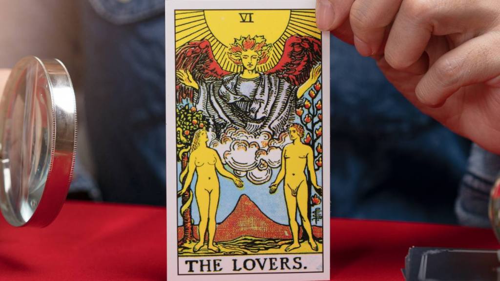 Fortuneteller holding Tarot fortune THE LOVERS card of one of the most popular occult Tarot on table.
