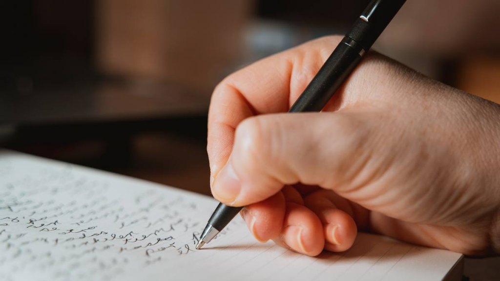 Woman's hand writing with a pen a text in a writer's notebook