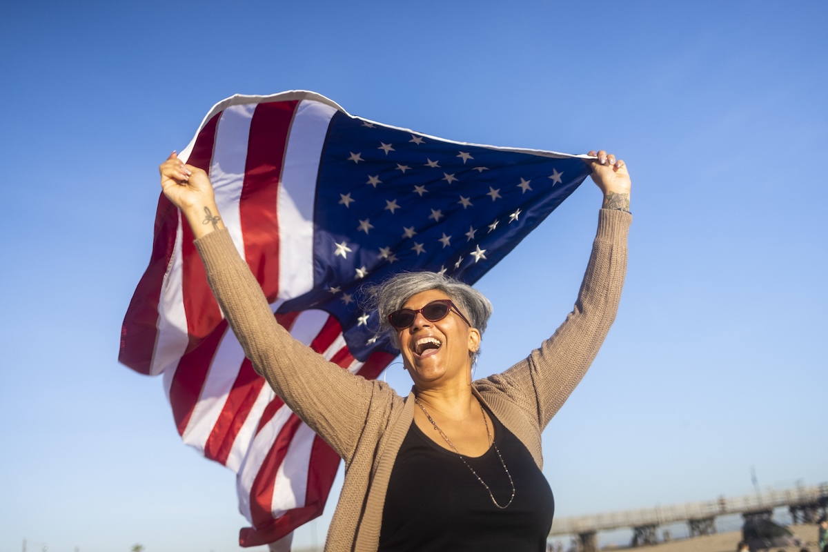 A happy woman carrying and waving an American Flag at the beach.