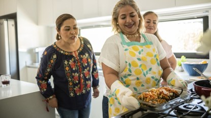 Three Mexican women preparing a dish for the oven in a clean bright modern kitchen