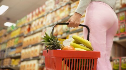 Woman stands in checkout line at the grocery store with basket full of produce