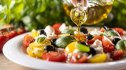 extra virgin olive oil is being poured on a plate of colorful vegetables