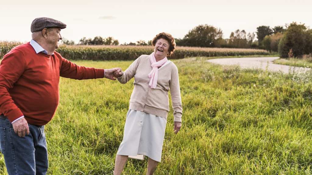 An old, happy couple dances outside.