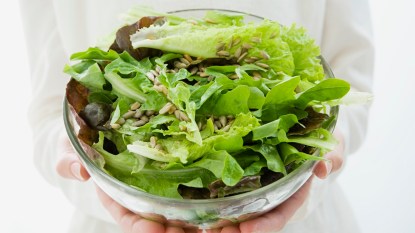 Person holding a glass bowl of green salad
