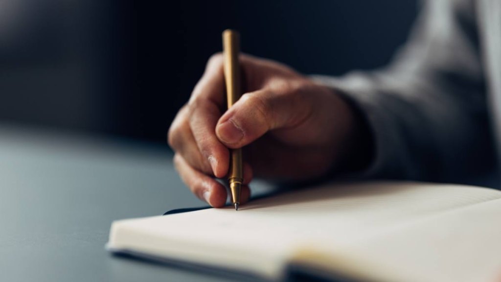 An individual meticulously jotting down notes in a notebook using an elegant pen, with a close-up on the writing hand.