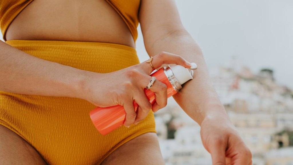 Close-up of a woman applying sun screen to her arm with a pump container.