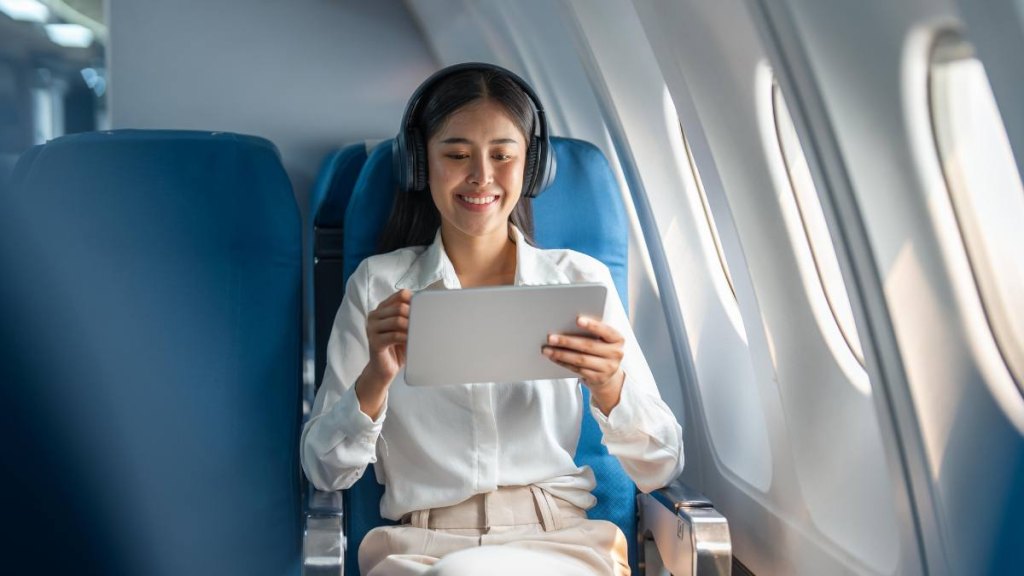 travel hacks for flying: Young Asian business woman or female passenger wearing wireless headphone and working with tablet during the flight.