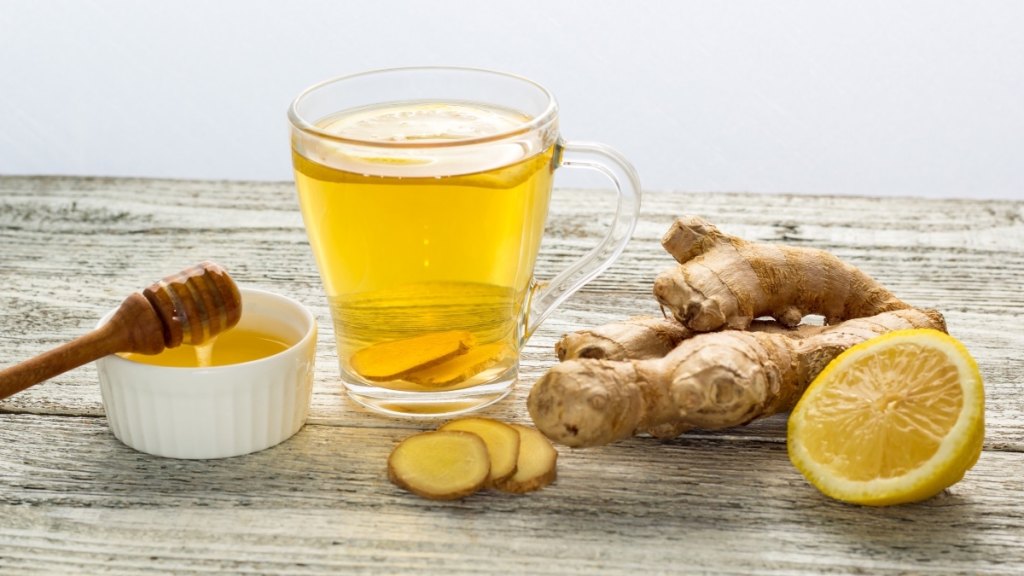 A cup of tea beside fresh ginger and honey, which can help eliminate common types of bad breath smells
