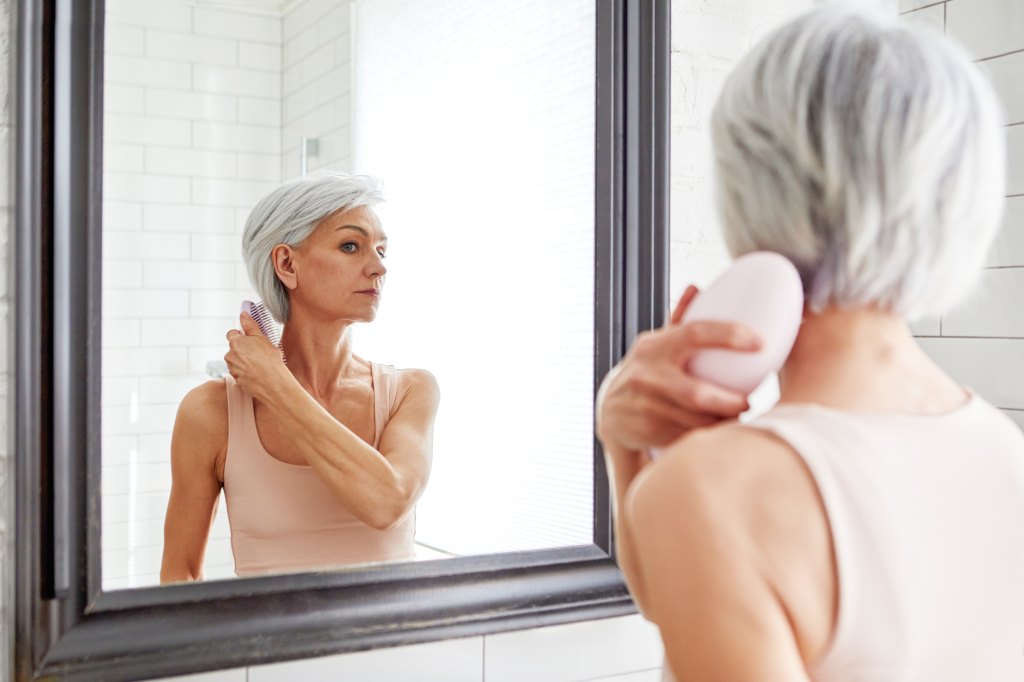 mature woman brushing hair in mirror