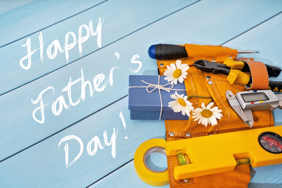 White text that reads 'Happy Father's Day' next to a tool belt on a table with daisies.