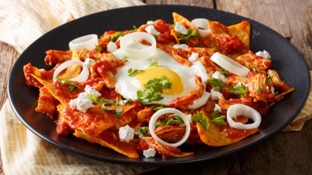 chilaquiles on plate with fried egg, salsa roja and onions