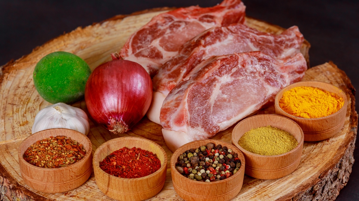 Raw strip steak with various spices on a wooden board top view