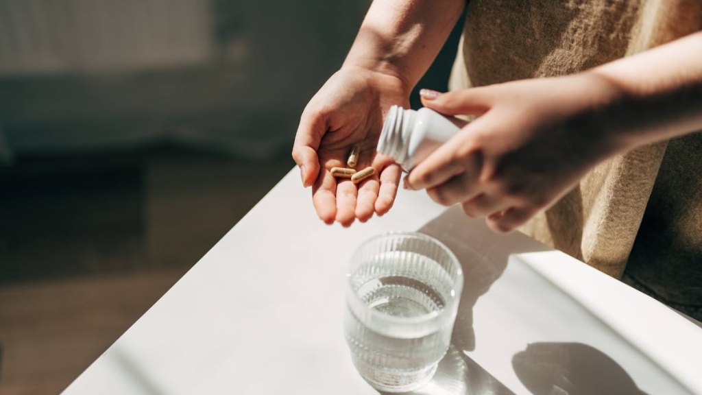 Hand with pills and water glass: what is colostrum