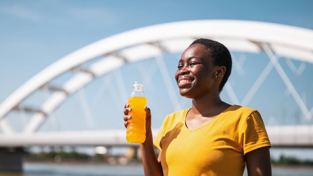 Mature woman in a yellow top holding a sports drink outdoors to treat her traveler's diarrhea