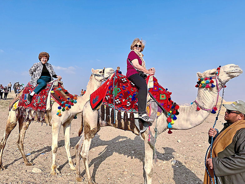 Senior travel buddies, Ellie and Sandy, riding camels in Egypt.