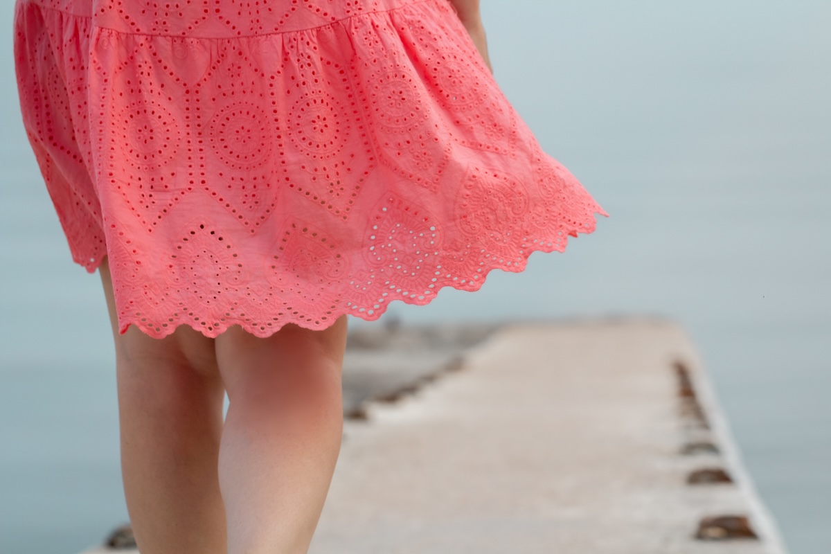 Close-up of pink summer sundress and female legs on the sea pier.