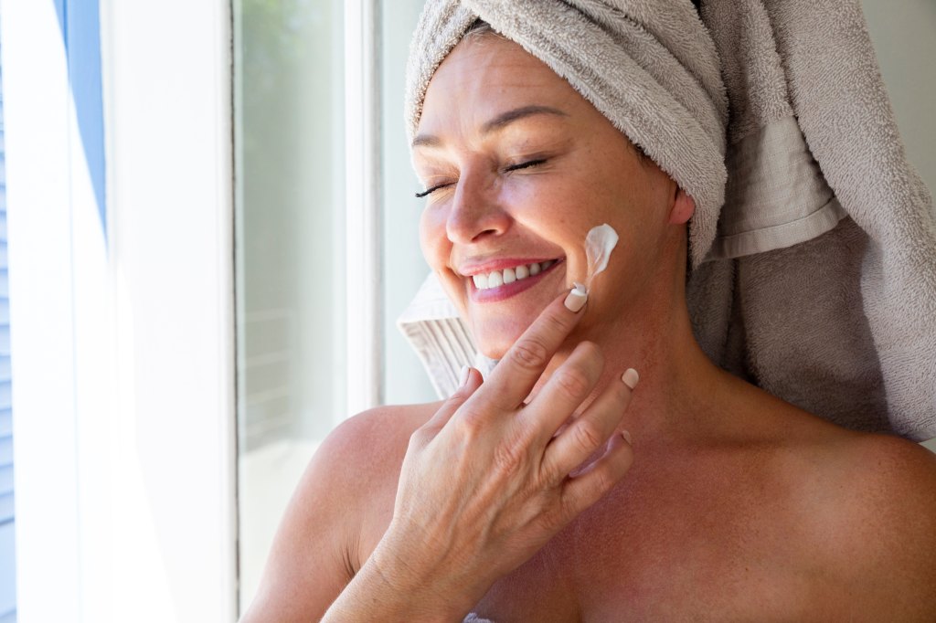 mature woman smiling applying sunscreen to face