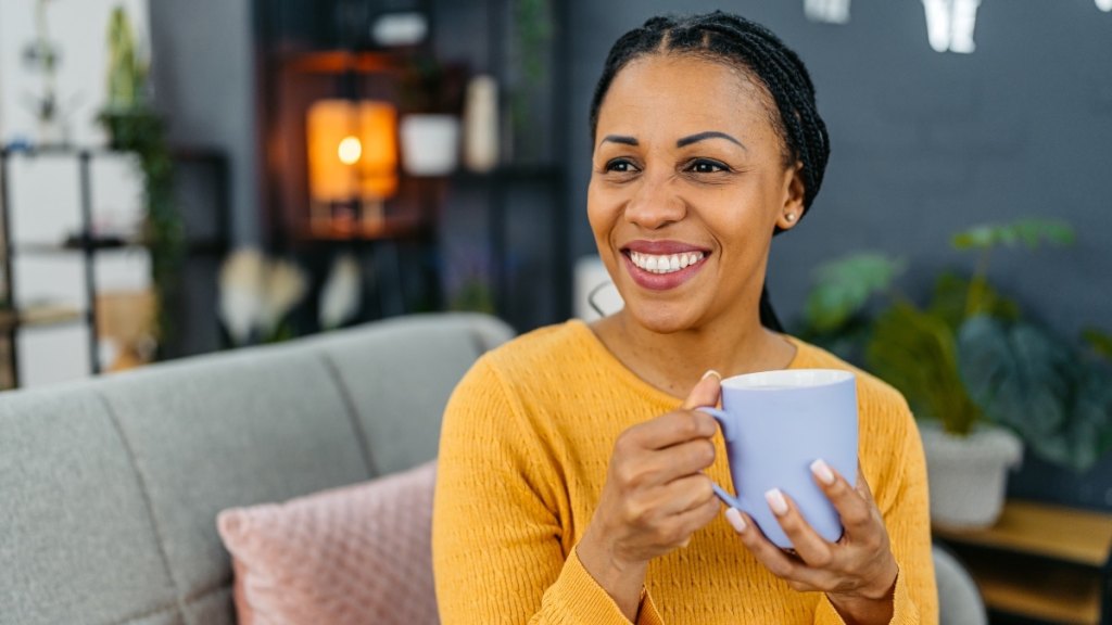 A mature woman sitting on her couch sipping a cup of oolong tea to get the health benefits