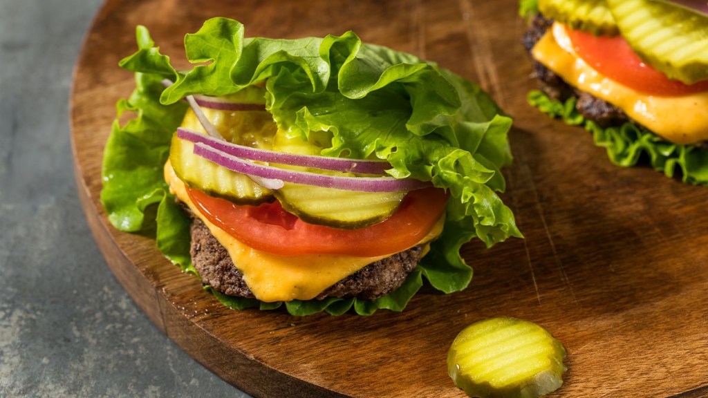 Burger with cheese, pickle, tomato and onion wrapped in lettuce for a keto meal 