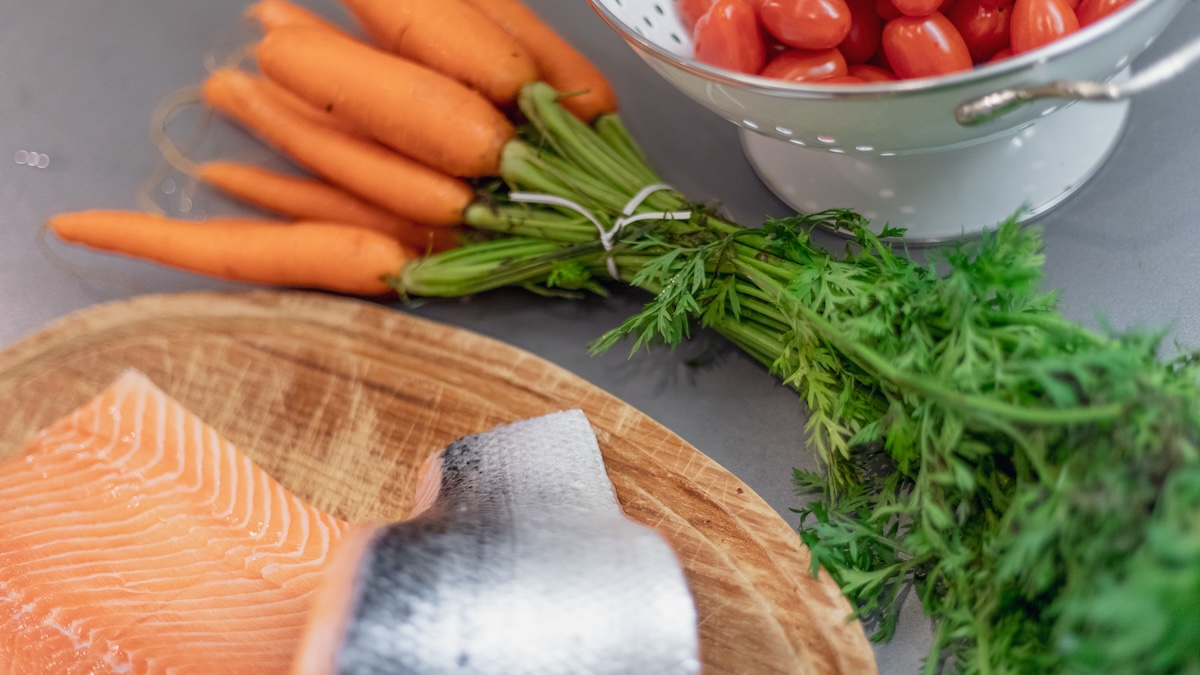 Delicious salmon fillet on wooden cutting board next to carrots and tomatoes.