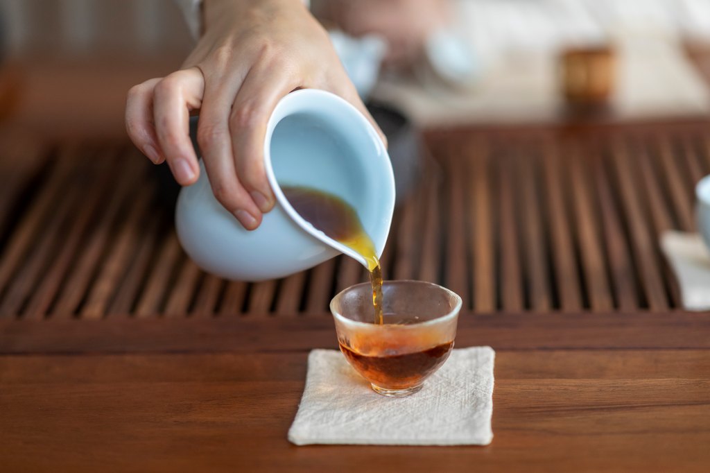 Close-up of human hands serving oolong tea in a glass, which has many health benefits