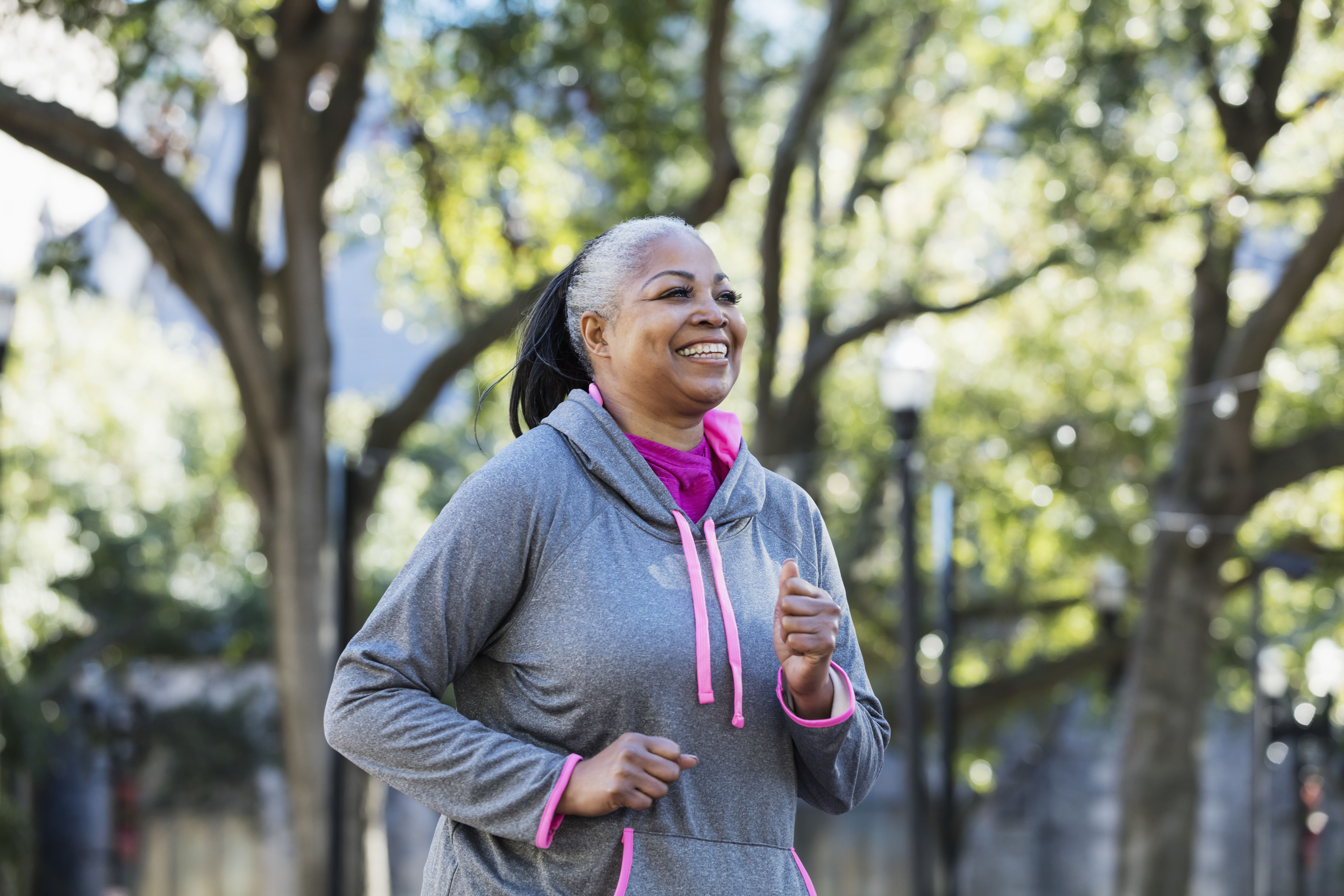 A mature African-American woman in her 50s wearing a hooded sweatshirt, smiling as she walks outside
