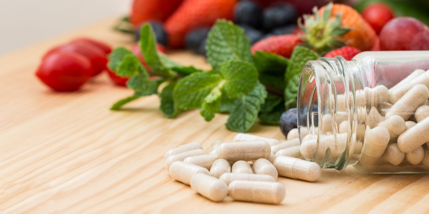 An image of white supplement pills in front of strawberries, radishes, and other fruits and vegetables.
