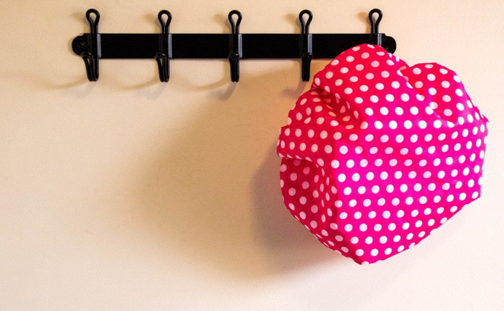 Pink polka dot shower cap hanging on hook for hair slugging.