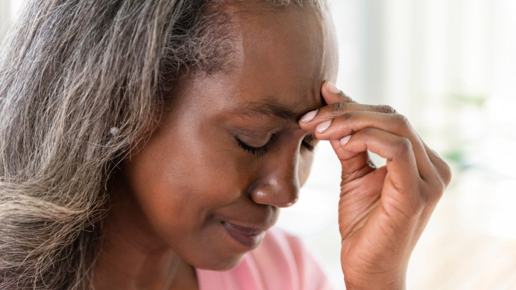 Mature woman closes her eyes and brings her hand to her head, as she suffers from a morning headache, a sign that helps answer her question: How do I know if I have sleep apnea?