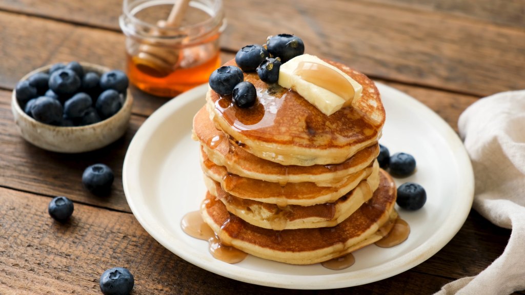pile of pancakes with butter, syrup and blueberries on plate