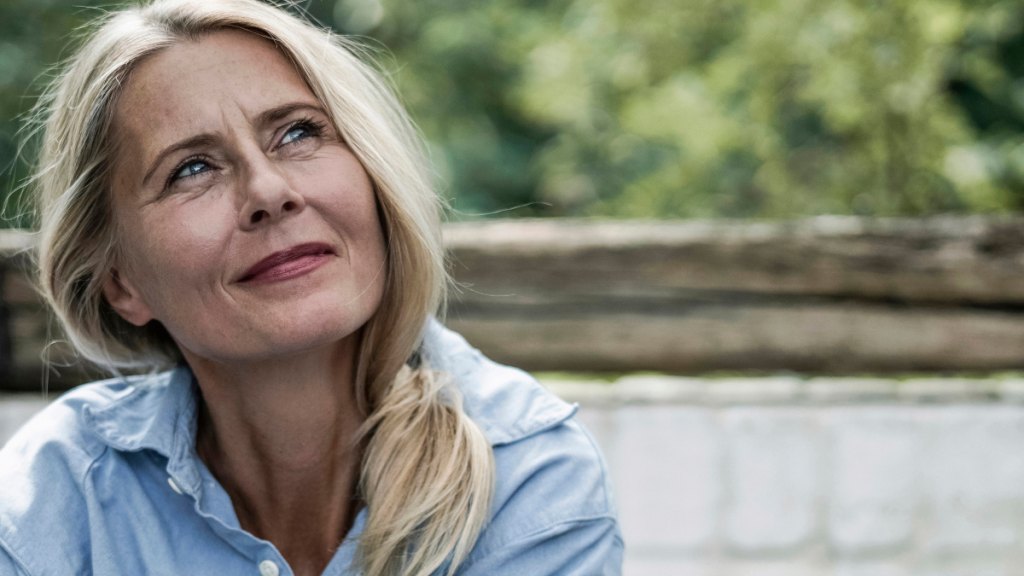middle-aged woman looks wistfully up at the heavens, a slight smile on her face