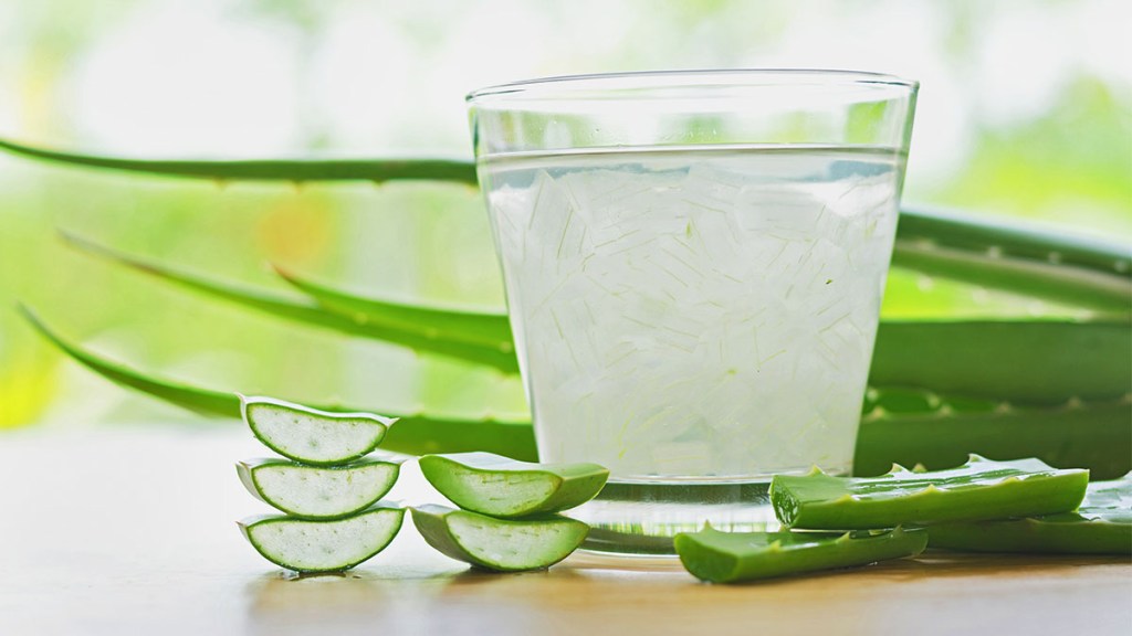 Glass of aloe vera juice surrounded by aloe leaves