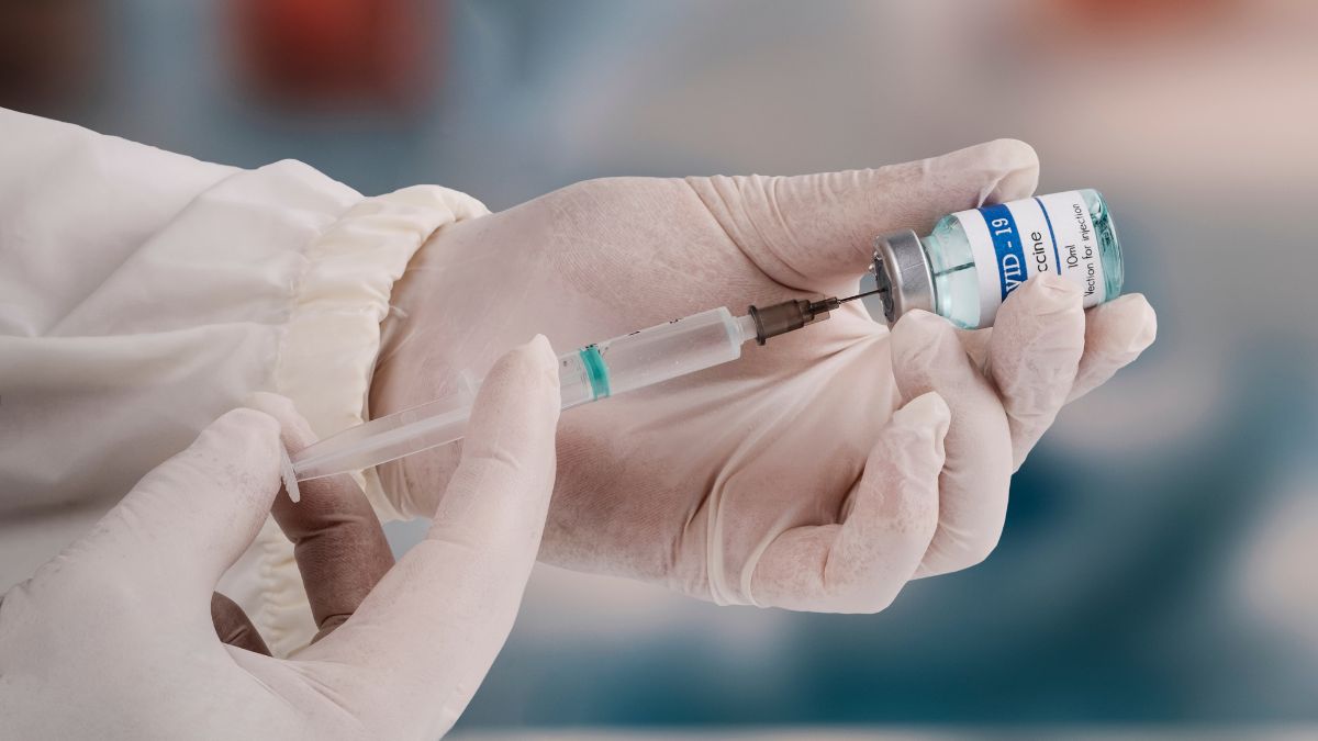 Using a syringe to attack the new covid-19 variant. A young doctor in a white protective glove holds a medical syringe and a vial.