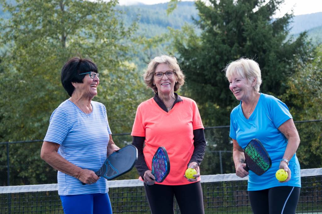 Three women laughing while playing a game of pickleball together
