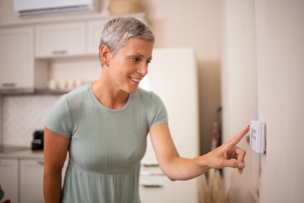 mature woman adjusts the temperature of thermostat at home for consistent sleep to help reduce her diabetes risk