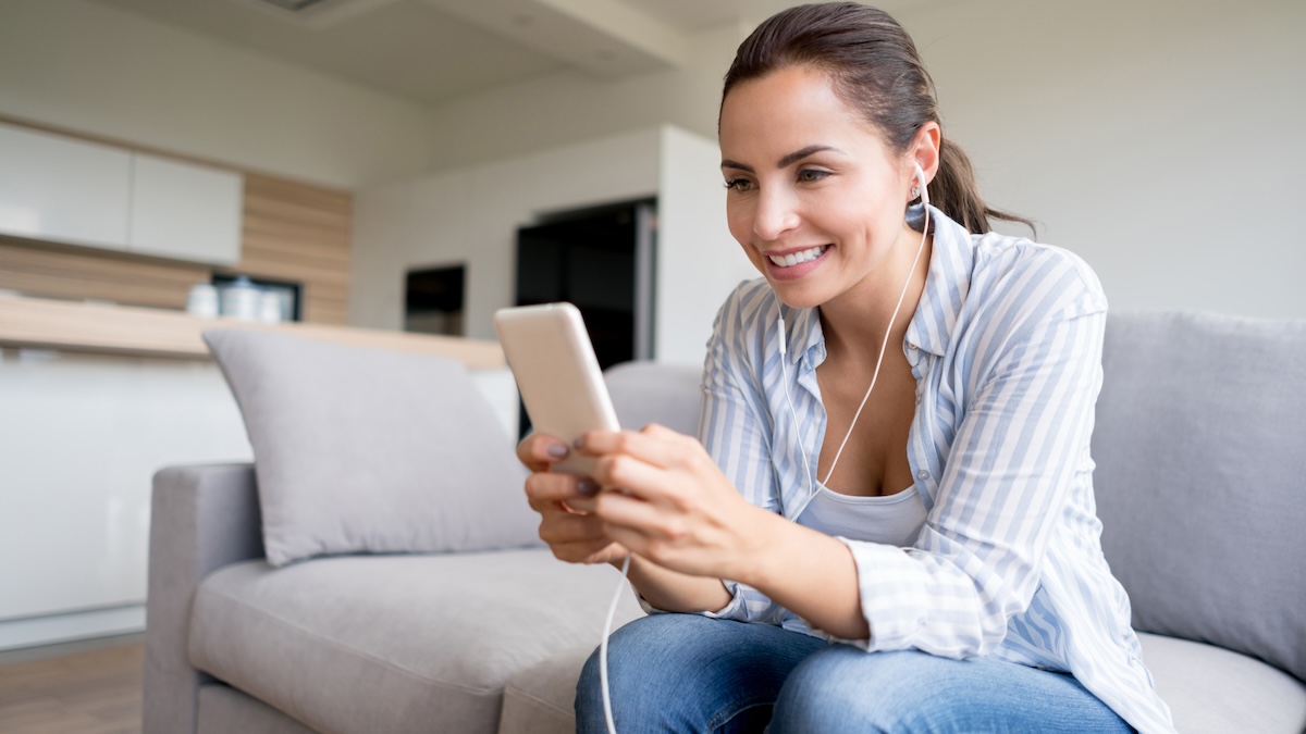 Woman at home listening to music on her cell phone with headphones – lifestyle