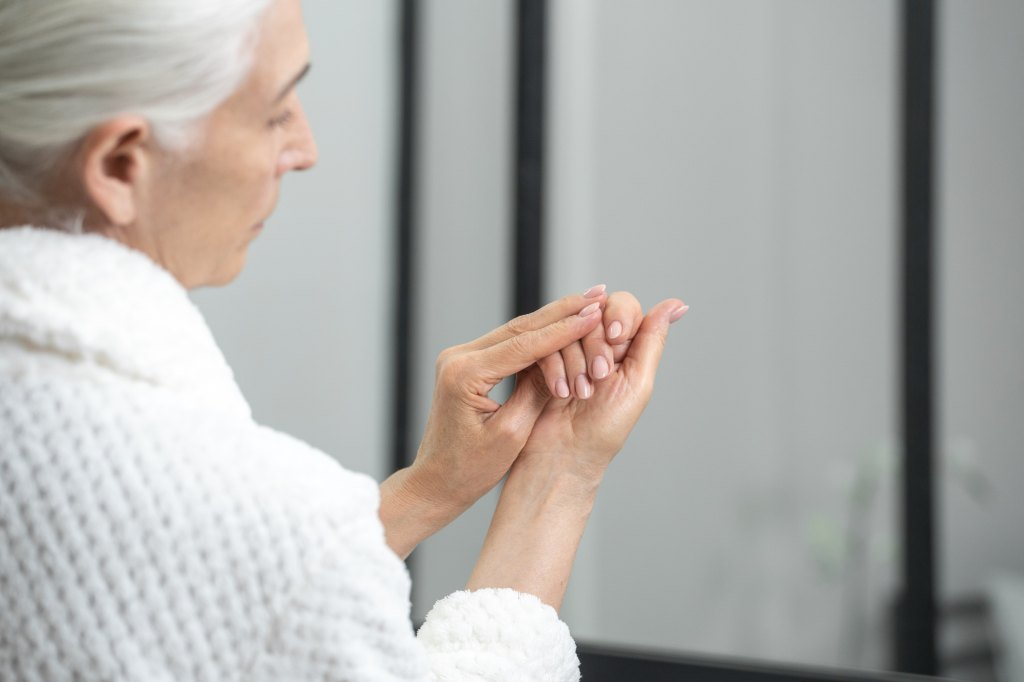mature woman in a robe inspecting her nails to get clues into her underlying health