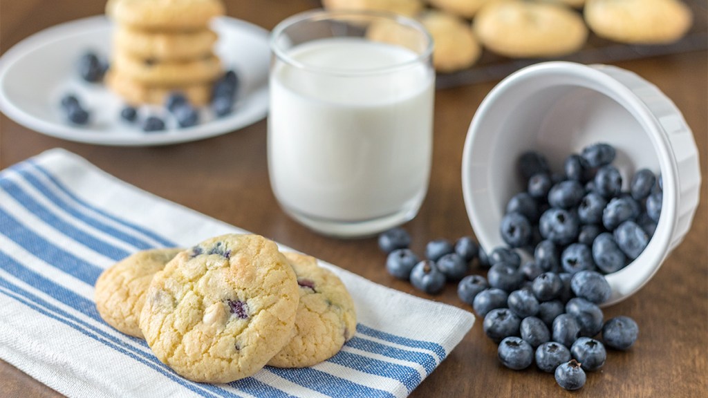 A spread of blueberry cookies, fresh blueberries and a glass of milk