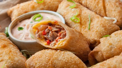 A pile of cheesesteak egg rolls served with dipping sauce