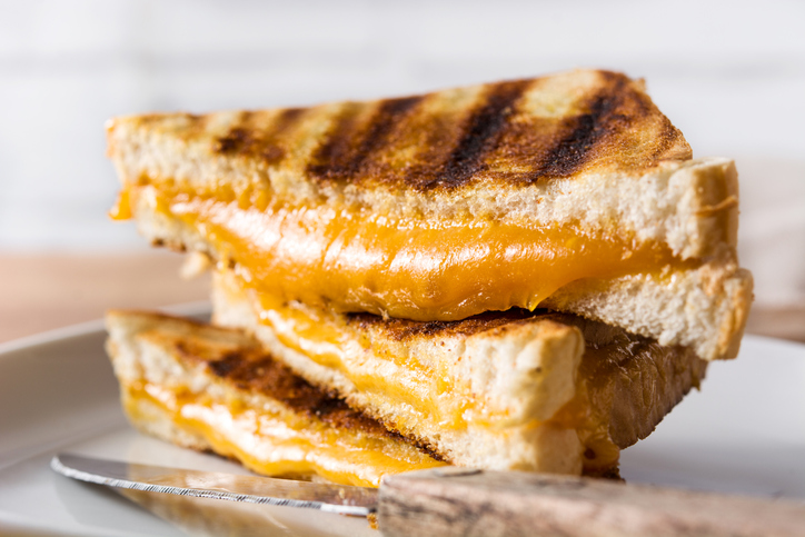 Closeup photo of toasted sandwich with melted cheese. Sandwich is on a white plate.