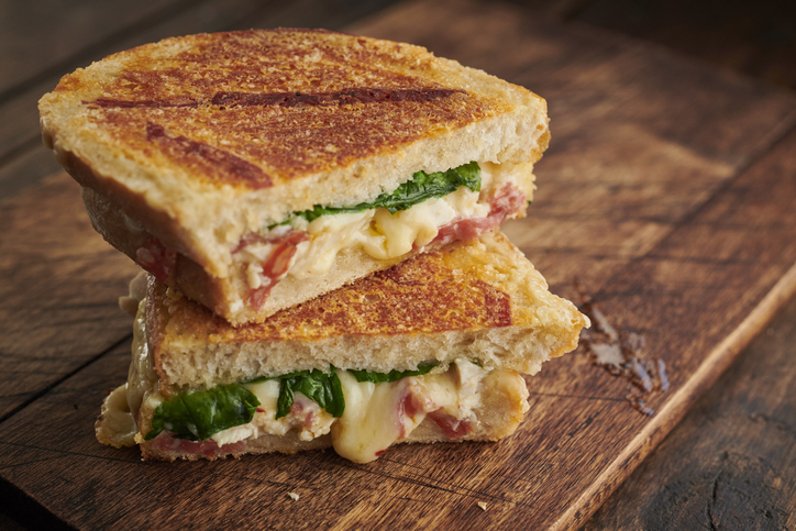 Grilled cheese sandwich with chicken and spinach stacked on a wooden table.