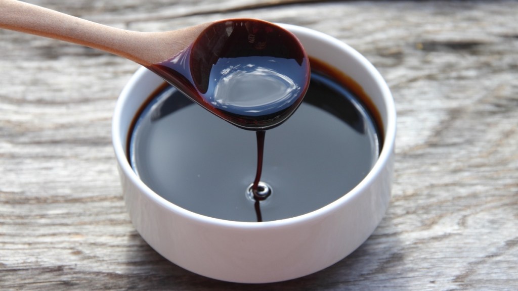 A white bowl of molasses with a wooden spoon