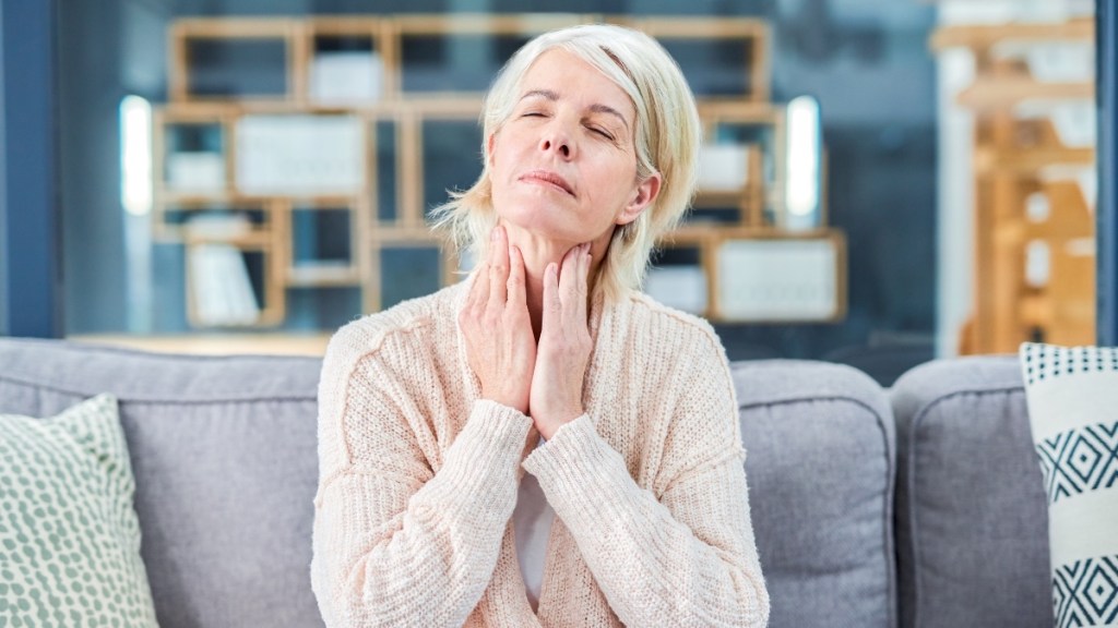 Woman with her hands touching her sore throat while sitting on the couch