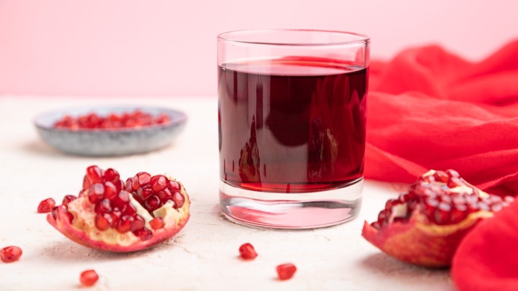 Glass of pomegranate juice next to arils, which can improve kidney function