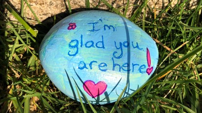 A rock painted with the words "I'm glad you're here" as a rock painting idea